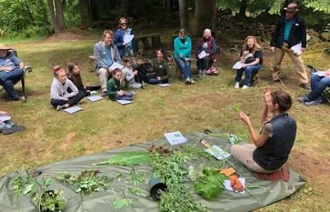 Nicole Apelian showing a variety of herbs to children in a garden setting, teaching them about the benefits of natural remedies with a warm and engaging demeanor.